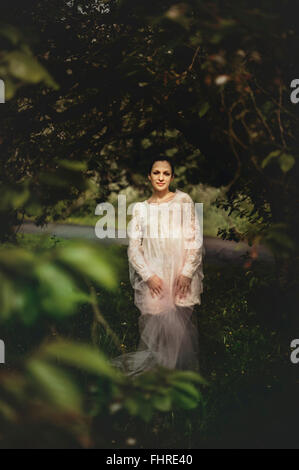 junge Frau trägt weißes Kleid stehend im Wald Stockfoto