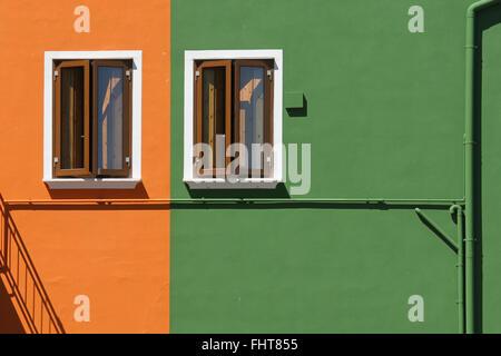 Ein Haus auf der Insel Burano nahe Venedig mit zwei identische Fenster und orange grün Malerei bei Tageslicht. Stockfoto