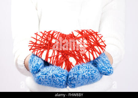 Warmen gekleidete Frau in ihren Händen in blaue Fäustlinge gestricktes rotes Herz hält. Symbol für Valentinstag Stockfoto