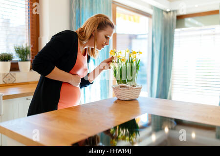 Schwangere Frau kümmert sich um Blumen in modernen Küche Stockfoto