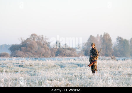 Jäger in Tarnung mit einer Schrotflinte auf seiner Schulter im Winter auf eine gefrorene Landschaft Rauchen Stockfoto