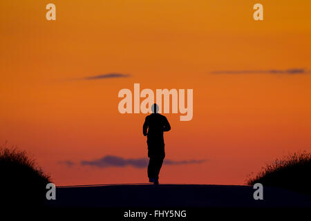 Einsamen Jogger laufen bei Sonnenuntergang Silhouette gegen orangefarbenen Himmel Stockfoto