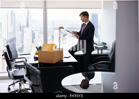 Geschäftsmann vor kurzem eingestellt für corporate Job zieht in sein neues Amt. Er nimmt einen Ordner aus einer Kiste und liest Dokumente Stockfoto