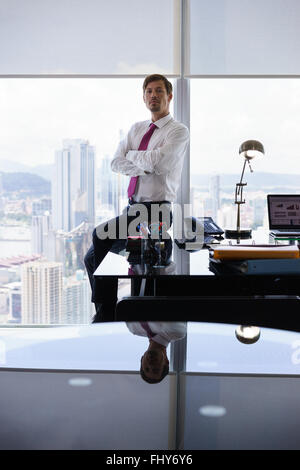 Erwachsenen Geschäftsmann sitzen im modernen Büro mit Blick auf die Stadt. Der Mann schaut die Kamera mit schweren Ausdruck Stockfoto