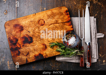 Hacken, schneiden Küche Board Salz Pfeffer und Rosmarin mit Gabel und Messer auf dunklem Holz schnitzen Stockfoto