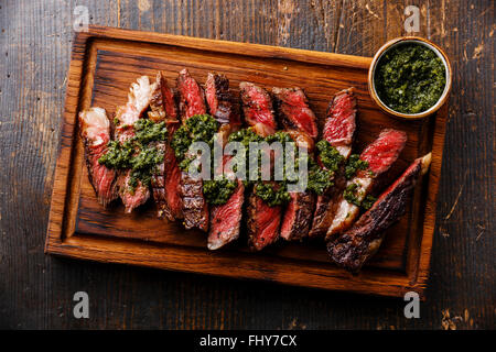 In Scheiben geschnitten mittlere seltene gegrilltes Rindfleisch Grill Ribeye Steak mit Chimichurri-Sauce auf Schneidebrett auf dunklem Hintergrund Stockfoto