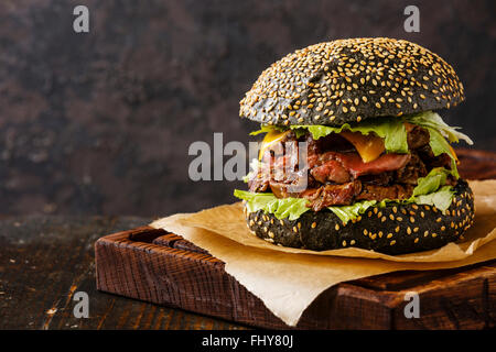 Roast Beef Burger auf Sesam Brötchen mit in Scheiben geschnittenen Pastrami auf schwarzem Hintergrund Stockfoto