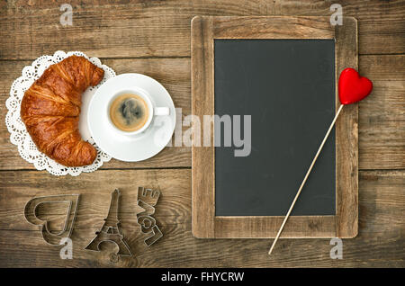 Schwarzer Kaffee mit Croissant, Blackboard und Herz Dekoration. Romantisches französisches Frühstück Stockfoto