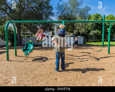 Vier junge Kinder Spaß auf einem riesigen Schwingen gesetzt, dass eine Erwachsenfrau sie auf Libbey Park, Ojai, Kalifornien schwingen ist. Stockfoto