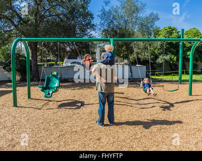 Vier junge Kinder Spaß auf einem riesigen Schwingen gesetzt, dass eine Erwachsenfrau sie auf Libbey Park, Ojai, Kalifornien schwingen ist. Stockfoto