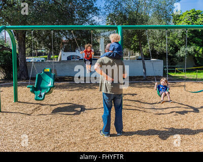 Vier junge Kinder Spaß auf einem riesigen Schwingen gesetzt, dass eine Erwachsenfrau sie auf Libbey Park, Ojai, Kalifornien schwingen ist. Stockfoto