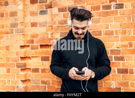 Porträt des jungen Mannes vor Ziegel Wand Musik hören mit Kopfhörern Stockfoto