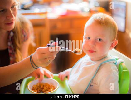 -MODELL VERÖFFENTLICHT. Mutter, Fütterung ihr Kleinkind in einen Hochstuhl. Stockfoto