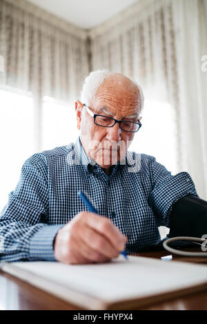 Ältere Mann seinen Blutdruck zu kontrollieren und das Ergebnis aufschreiben Stockfoto