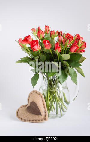 Rote Blumen in transparentem Glas mit Herz auf weißem Hintergrund Stockfoto