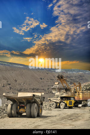 Bagger laden von Eisenerz in schwere Muldenkipper auf den Tagebau auf Sonnenuntergang Stockfoto