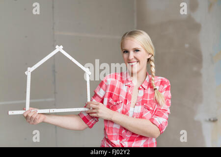 Lächelnde junge Frau hält Tasche Regel in Form eines Hauses auf Baustelle Stockfoto