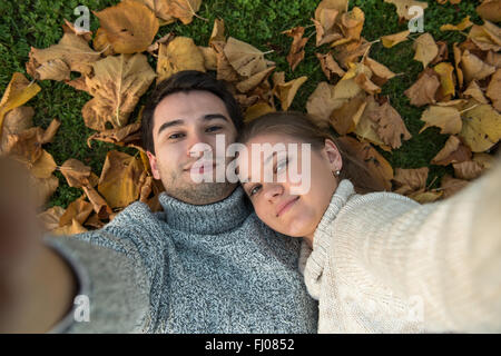 junges Paar im Park, in der Liebe, so dass Selfie, liegend auf den grünen Rasen und gelbe Blätter Stockfoto