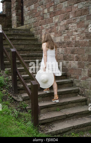 Frau in weißem Kleid, einen Hut, Klettern die Treppe im Freien halten Stockfoto