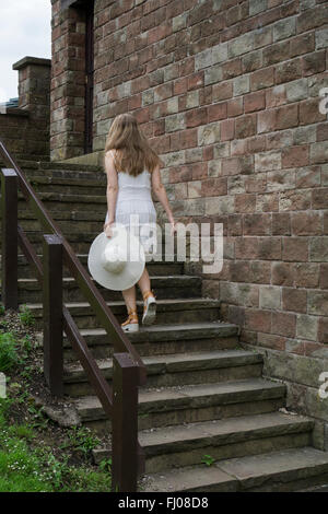 Frau in weißem Kleid, einen Hut, Klettern die Treppe im Freien halten Stockfoto