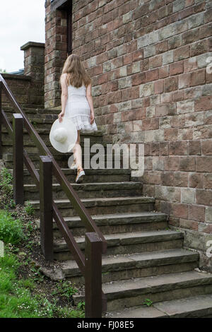 Frau in weißem Kleid, einen Hut, Klettern die Treppe im Freien halten Stockfoto