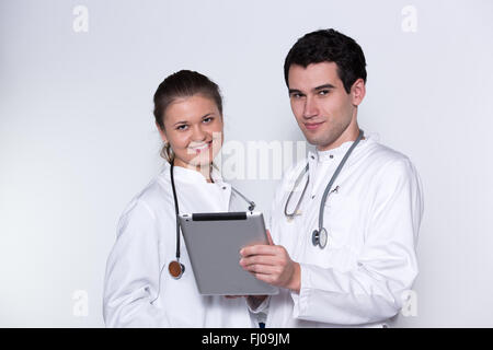 zwei junge Ärzte, männlich und weiblich in weißen Kitteln mit Stethoskop mit Tablet-pc arbeiten Stockfoto