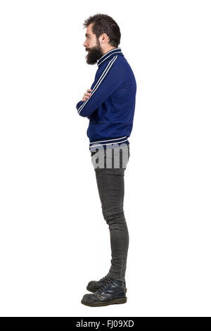 Seitenansicht des bärtigen punker in blauem Trainingsanzug Jacke mit verschränkten Armen wegsehen. Ganzkörper-Länge-Porträt isoliert auf weiss Stockfoto