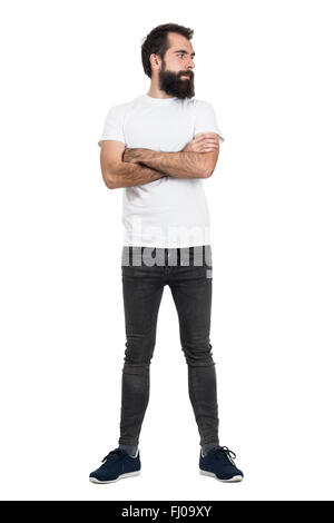 Ernsthafte bärtige Hipster in weißem T-shirt und enge Jeans wegsehen. Ganzkörper-Länge-Porträt isoliert auf weißem Hintergrund Stockfoto