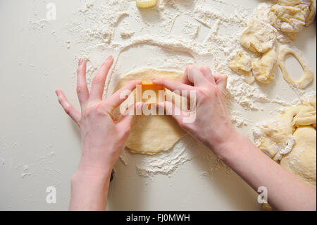 Nahaufnahme von weiblichen Händen machen Cookies aus frischem Teig zu Hause. Teig, Mehl, Backformen auf einem weißen Tisch im Hintergrund. Stockfoto