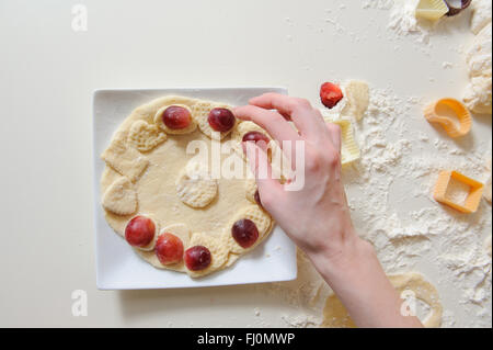 Nahaufnahme von weiblichen Händen machen Cookies aus frischem Teig zu Hause. Teig, Mehl, Backformen auf einem weißen Tisch im Hintergrund. Stockfoto