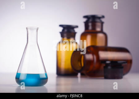 Eine medizinische Glas mit blauer Flüssigkeit vor alte braune Gläser Stockfoto