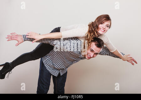 Lächelnde Frau Reiten Huckepack auf Schultern Mannes. Glückliches junges Paar Spaß zusammen im Studio auf grau. Stockfoto