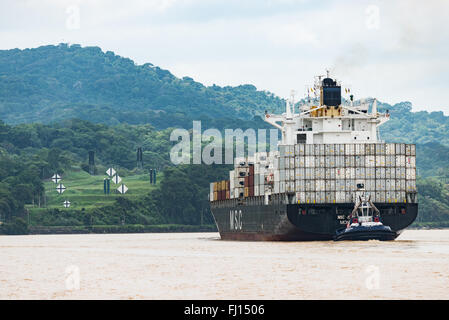 Panama-Kanal Containerschiff Schlepper Panama | PANAMA-KANAL, Panama — Ein Schlepper geleitet ein großes Containerschiff entlang eines engen Abschnitts des Panama-Kanals. Der etwa 50 Meilen (80 km) lange Wasserweg, der 1914 fertiggestellt wurde, verbindet den Atlantik und den Pazifik über die Landenge von Panama und erspart Schiffen die lange Reise um Südamerika. Die Vereinigten Staaten bauten und betrieben den Kanal, bis sie die Kontrolle am 31. Dezember 1999 im Rahmen der Torrijos-Carter-Verträge an Panama übergaben. Seitdem verwaltet die Panama Canal Authority den Wasserweg, einschließlich der Überwachung einer großen Erweiterung, die am 26. Juni 2016 eingeweiht wurde Stockfoto