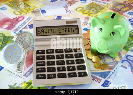 Taschenrechner mit den Worten spart Kraft, zwei LED-Lampen und ein grünes Sparschwein auf einem Hintergrund gemacht von Euro-Banknoten Stockfoto