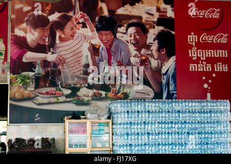 Kunststoff-Flaschen sind unter einem großen Coca Cola Werbung Schild in einem Restaurant in Skun, Provinz Kampong Cham, Kambodscha gestapelt. Stockfoto