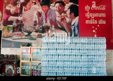 Kunststoff-Flaschen sind unter einem großen Coca Cola Werbung Schild in einem Restaurant in Skun, Provinz Kampong Cham, Kambodscha gestapelt. Stockfoto