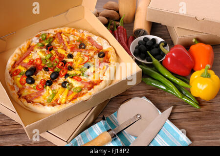 Frisch gebackene Pizza in einer Lieferbox umgeben von verschiedenen Zutaten auf einem Tisch oder Arbeitsplatte. Stockfoto