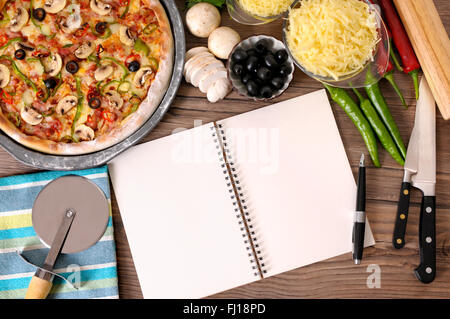 Frisch gebackene Pizza mit leeren Notebook oder Kochbuch umgeben von verschiedenen Zutaten. Stockfoto