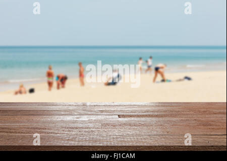 Holz Tischplatte auf verschwommene blaue Meer und weißen Sandstrand mit einigen Leuten - für die Anzeige verwendet werden oder die montage Ihrer Produkte Stockfoto