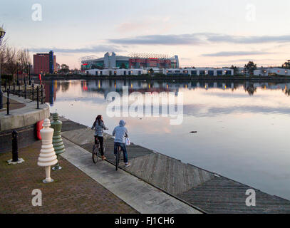 Zeigen Sie zwei Jugendliche auf Fahrrädern, ein Junge und ein Mädchen Old Trafford Stadion, Heimat des Manchester United Football Club, von Salford Quays an Stockfoto