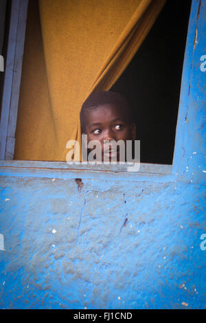 Schwarze afrikanische Kind schaut durch ein Fenster mit blauen Wand in Jinka, Äthiopien Stockfoto