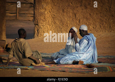 Drei Männer sprechen in Djenné, Mali, auf dem Boden sitzend am frühen Morgen mit der traditionellen Kleidung Stockfoto