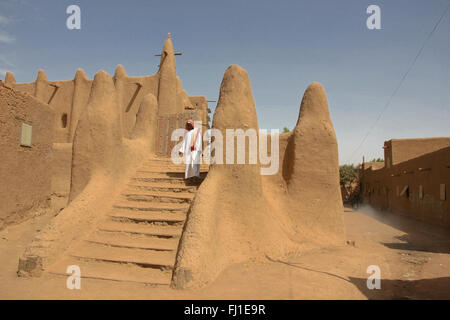 Ein Mann mit traditioneller Kleidung geht aus dem atemberaubenden Schlamm banco heiligen Moschee in Djenné, Mali, Afrika Stockfoto