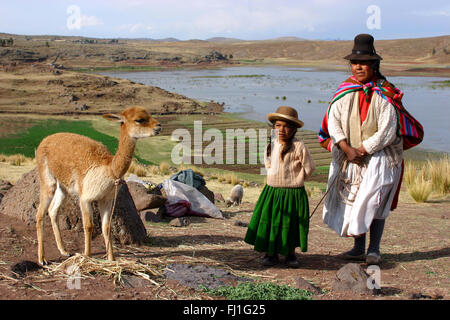 Peruanische Mutter mit ihrer Tochter und ihrem Lama (oder Alpaga) in Sillustani, Peru Stockfoto