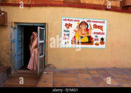 Eine Frau steht am Eingang eines Hauses in Jaisalmer Fort, mit der Malerei des hinduistischen Gottes Ganesh auf der Wand, Jaisalmer, Indien Stockfoto