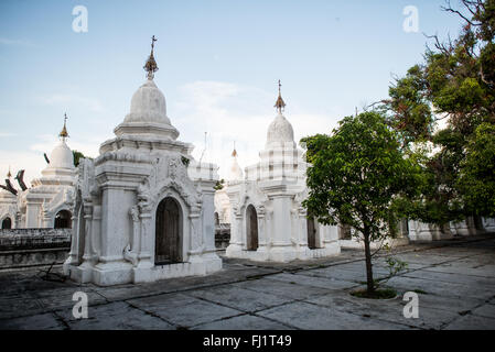 MANDALAY, Myanmar – Reihen von unberührten weißen Kyauksa gu (Höhlen mit Steininschriften) erstrecken sich über das Gelände der Kuthodaw-Pagode. Der 1857 von König Mindon erbaute Komplex enthält 729 Marmorplatten, die zusammen das als das größte Buch der Welt bekannt ist. Jede kleine Stupa beherbergt eine Marmortafel auf beiden Seiten mit Text aus dem Tipitaka, dem vollständigen Pali-Kanon des Theravada-Buddhismus. Die geordnete Anordnung dieser Strukturen spiegelt traditionelle buddhistische Architekturprinzipien wider. Stockfoto