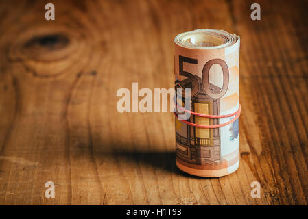 Konzept Geld sparen bares Geld mit Gummiband auf hölzernen Schreibtisch, fünfzig Euro Banknoten persönliche Haushaltsbudget Stack aufgerollt Stockfoto