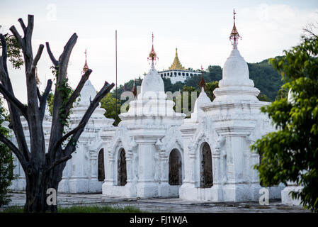 MANDALAY, Myanmar – Reihen von unberührten weißen Kyauksa gu (Höhlen mit Steininschriften) erstrecken sich über das Gelände der Kuthodaw-Pagode. Der 1857 von König Mindon erbaute Komplex enthält 729 Marmorplatten, die zusammen das als das größte Buch der Welt bekannt ist. Jede kleine Stupa beherbergt eine Marmortafel auf beiden Seiten mit Text aus dem Tipitaka, dem vollständigen Pali-Kanon des Theravada-Buddhismus. Die geordnete Anordnung dieser Strukturen spiegelt traditionelle buddhistische Architekturprinzipien wider. Stockfoto