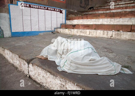 Man schläft unter einem großen weißen Blatt auf einem GHAT von Varanasi, Indien Stockfoto