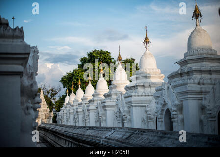 MANDALAY, Myanmar – Reihen von unberührten weißen Kyauksa gu (Höhlen mit Steininschriften) erstrecken sich über das Gelände der Kuthodaw-Pagode. Der 1857 von König Mindon erbaute Komplex enthält 729 Marmorplatten, die zusammen das als das größte Buch der Welt bekannt ist. Jede kleine Stupa beherbergt eine Marmortafel auf beiden Seiten mit Text aus dem Tipitaka, dem vollständigen Pali-Kanon des Theravada-Buddhismus. Die geordnete Anordnung dieser Strukturen spiegelt traditionelle buddhistische Architekturprinzipien wider. Stockfoto